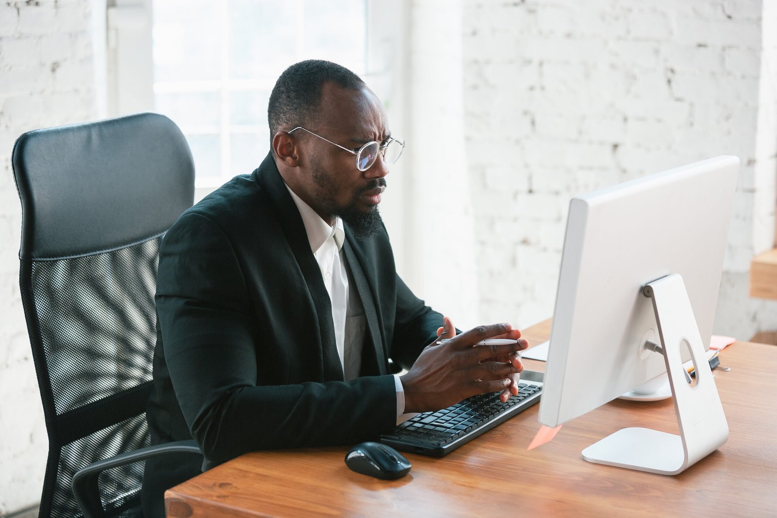 Typing text. African-american entrepreneur, businessman working concentrated in office. Looks serios and busy, wearing classic suit, jacket. Concept of work, finance, business, success, leadership.